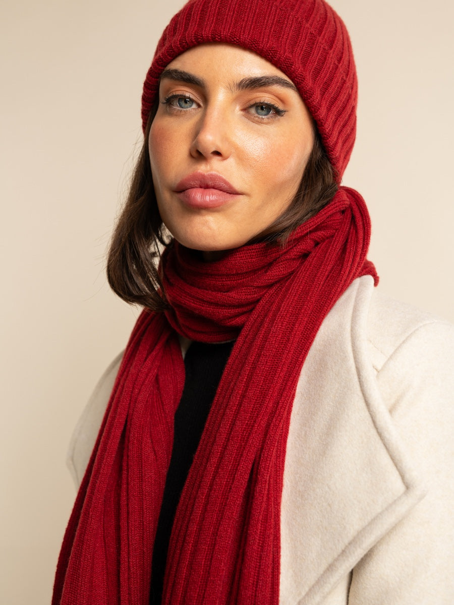 Woman wearing a red cashmere knit hat and scarf against a beige background