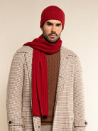 Man wearing a red knit hat and scarf with a patterned coat on a beige background