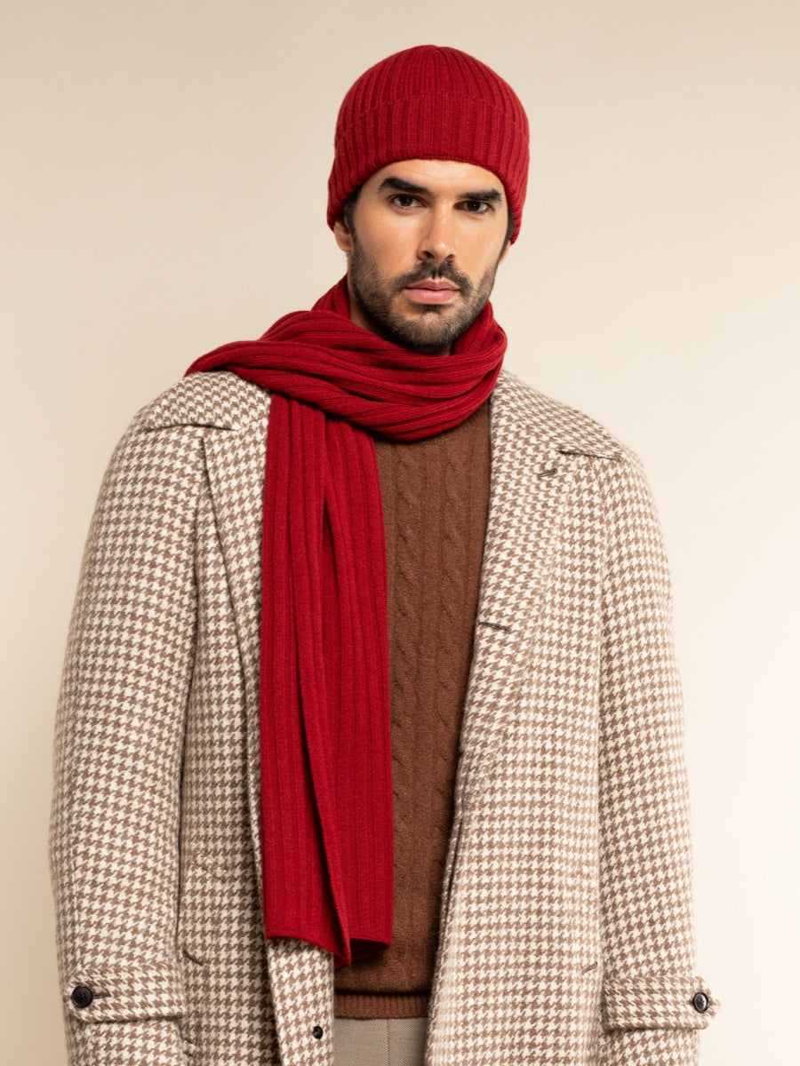 Man wearing a red knit hat and scarf with a patterned coat on a beige background