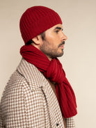 Man wearing a red knit beanie and scarf against a beige background