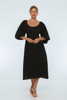 Woman wearing a black midi dress with puff sleeves and scoop neck on a white background