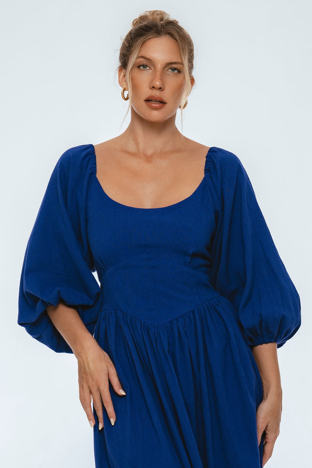 Woman wearing a blue dress with puffed sleeves on a light gray background
