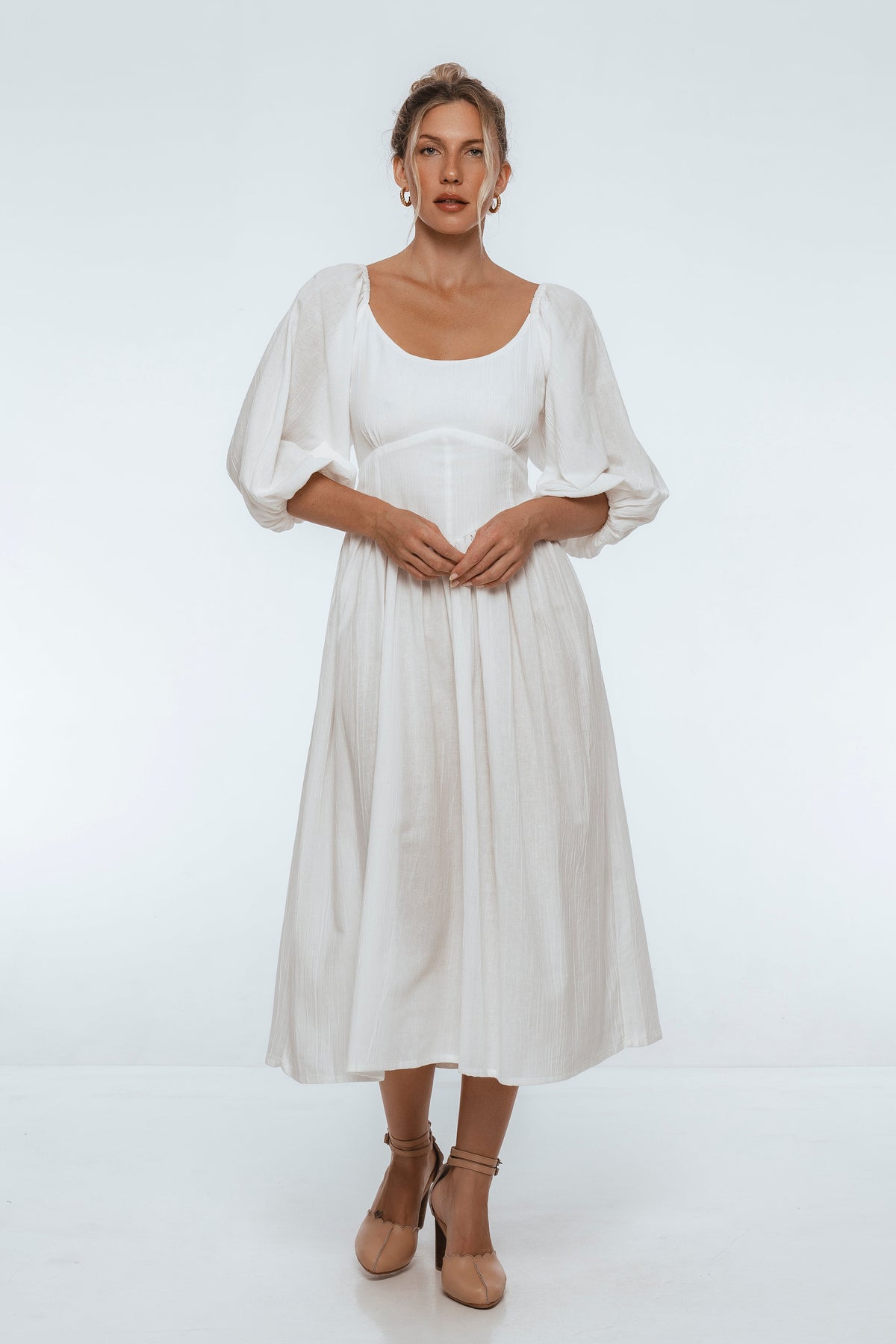 Woman wearing a white midi dress with puff sleeves on a white background