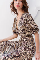 Woman wearing a beige patterned wrap dress with deep v-neckline against a white background