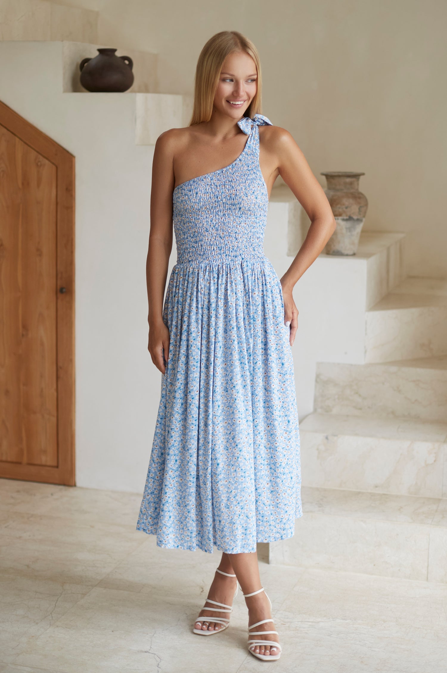 Woman wearing blue floral one-shoulder dress with a fitted bodice, smocked at the bust, midi length, front view