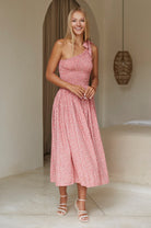 Woman wearing pink floral one-shoulder dress with a fitted bodice, smocked at the bust, midi length, front view