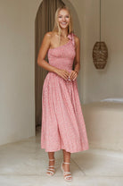 Woman wearing a pink floral one-shoulder midi dress in a neutral setting, front view.