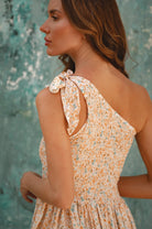 Woman wearing a cream floral dress with a textured green background, back view