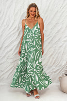 Woman wearing an orange colorful patterned flowy maxi dress with deep v-neckline and spaghetti straps against a white textured wall.