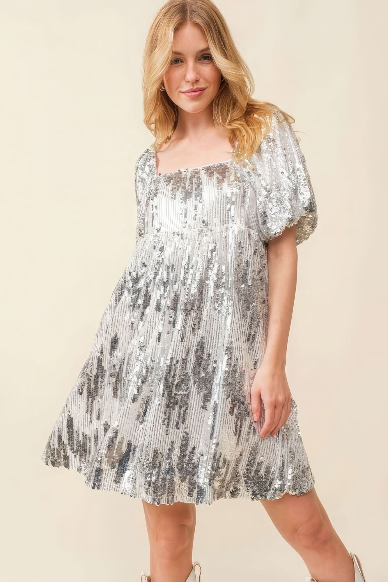Close-up front view of square neckline and puff sleeves on silver sequin mini dress.
