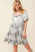 Close-up front view of square neckline and puff sleeves on silver sequin mini dress.
