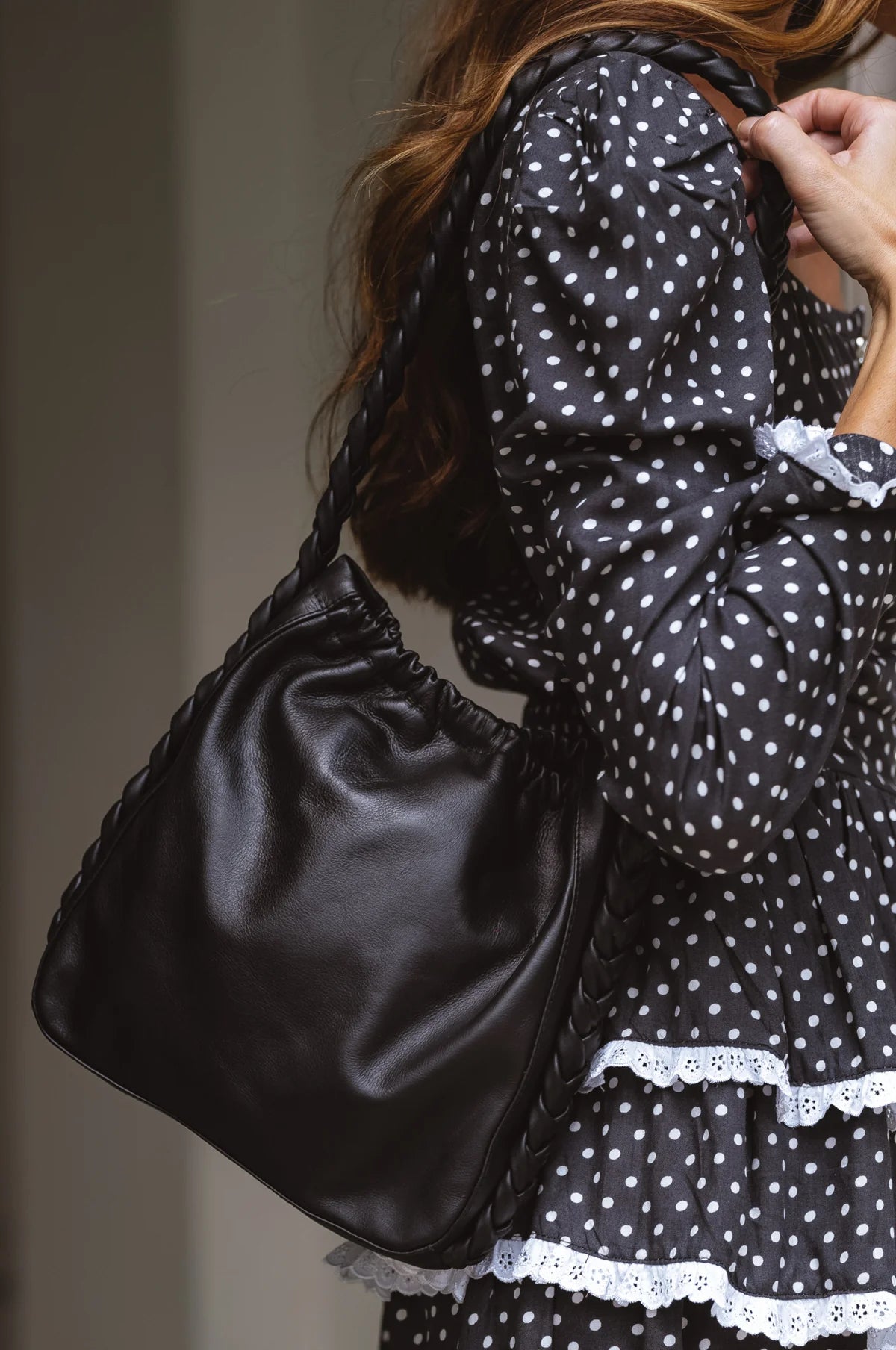 Side view of the Sivuple Leather Shoulder Bag in black worn over the shoulder with a black polka dot dress.