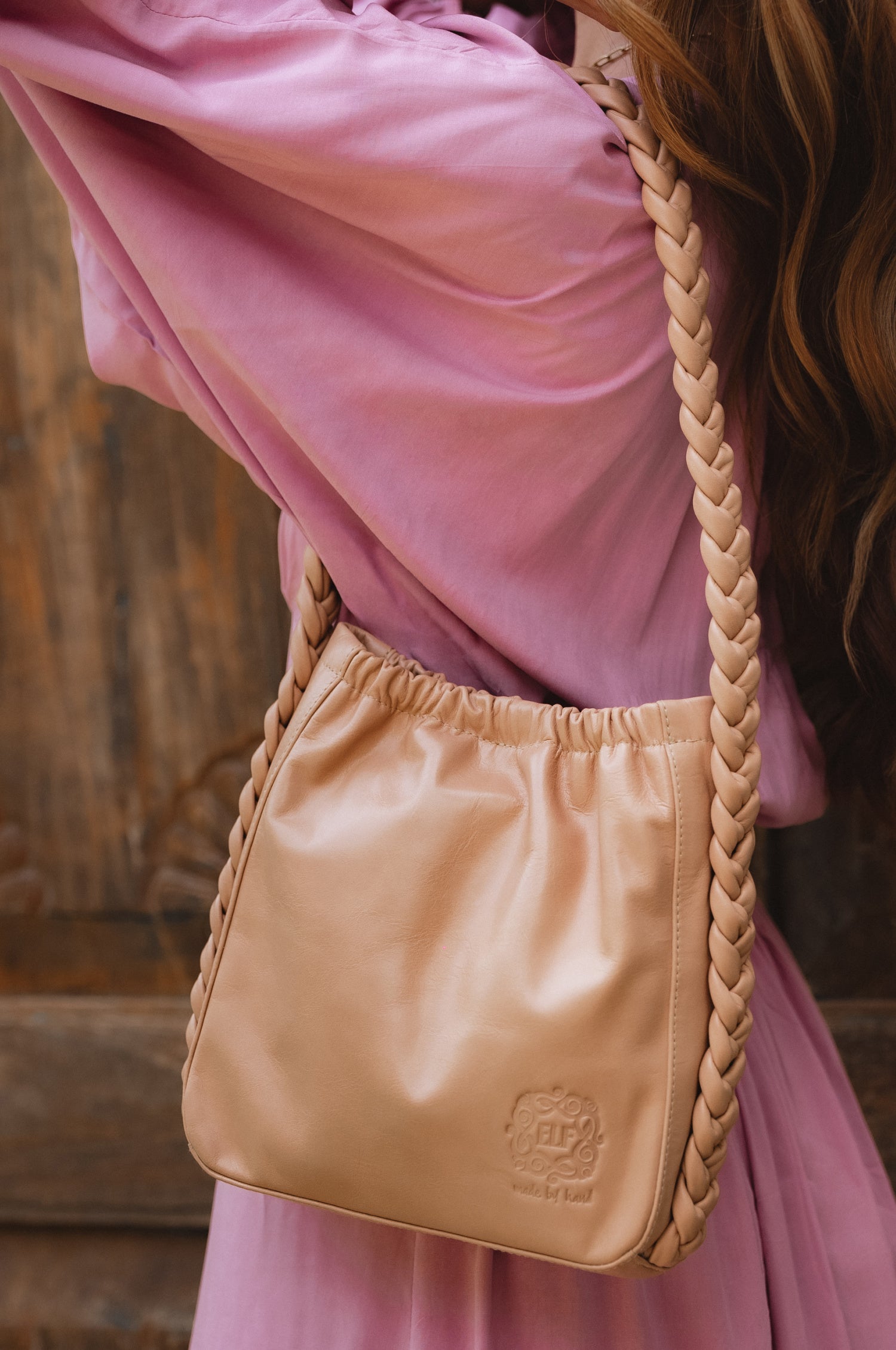 Model wearing the Sivuple Leather Shoulder Bag in vintage beige over a mauve dress, highlighting the braided leather shoulder strap and bucket silhouette.
