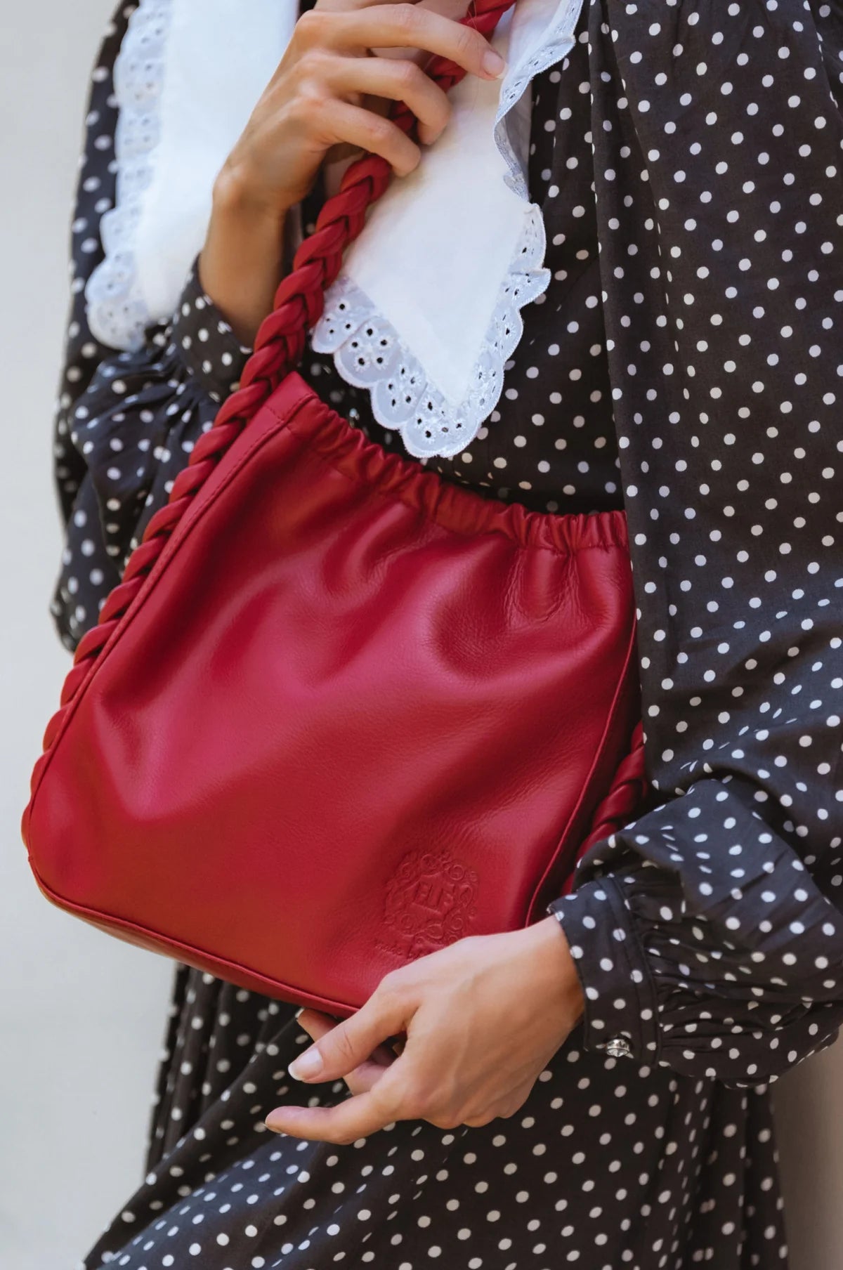 Close up of the Sivuple Leather Shoulder Bag in vintage red styled with a black polka dot dress and white lace collar.