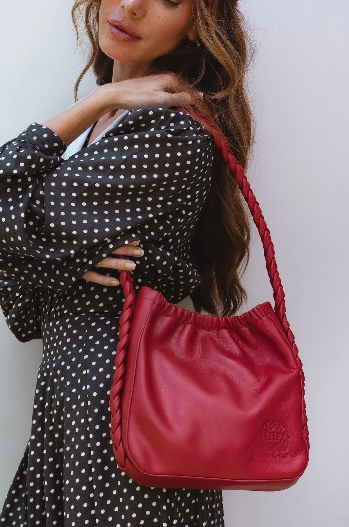 Model carrying the Sivuple Leather Shoulder Bag in vintage red with a black polka dot dress, highlighting the braided leather shoulder strap.