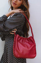 Model carrying the Sivuple Leather Shoulder Bag in vintage red with a black polka dot dress, highlighting the braided leather shoulder strap.