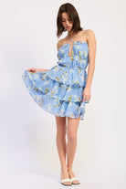 Woman wearing a blue floral ruffle tiered mini dress against a white background front view