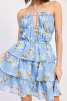 Woman wearing a blue floral ruffle tiered mini dress against a white background front view