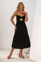 Woman wearing a black midi dress with spaghetti straps and cut-out design in a minimalistic setting