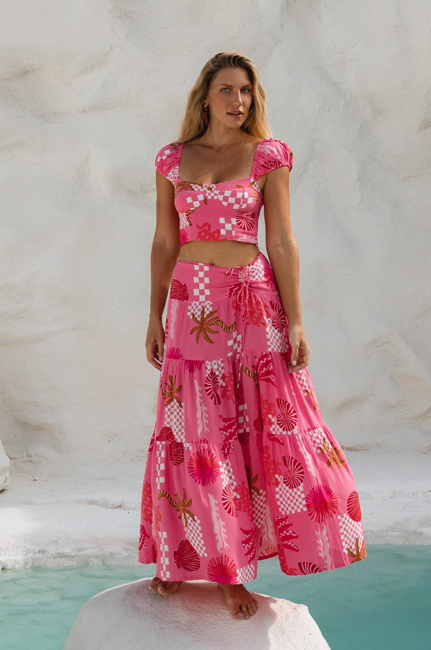 Woman wearing a pink and white patterned matching two-piece cropped top and maxi skirt against a textured marble background