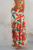 Woman wearing a floral two-piece cropped top with maxi skirt with red and green patterns on a white background, back view