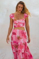 Woman wearing a pink, white and magenta abstract floral and shell motif cropped top two-piece outfit against a white background