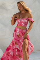 Woman wearing a pink, white and magenta abstract floral and shell motif cropped top with flutter sleeve worn off the shoulder and matching skirt with white background, front view