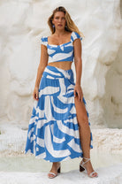 Woman wearing a blue and white patterned matching two-piece cropped top and maxi skirt with high slit against a textured white background