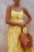 Woman wearing a yellow dress holding a tan leather bag against a neutral background