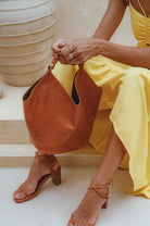 Person wearing a yellow dress and brown sandals, holding a tan soft leather handbag.
