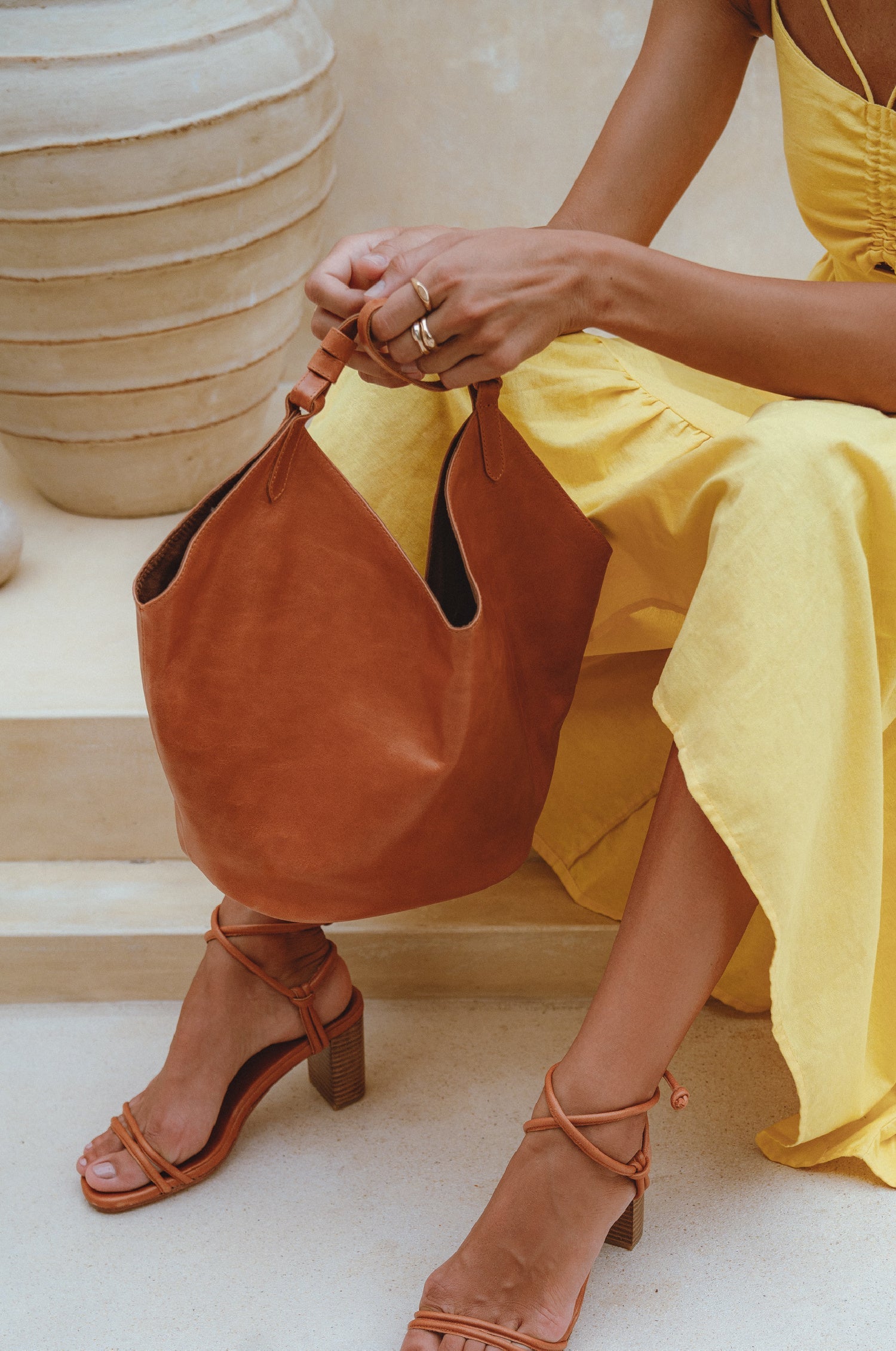Person wearing a yellow dress and brown sandals, holding a tan soft leather handbag.