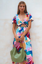 Woman wearing a colorful floral dress holding a green leather handbag against a light background