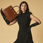 Woman holding a brown leather handbag against a beige background