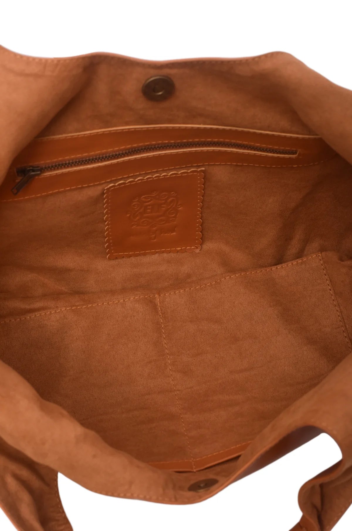 Close-up of the tan suede lined interior of a tan leather bag, showing a zippered pocket, a stitched interior pocket, and a small, embossed brand patch on the lining.