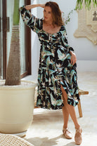 Woman in a floral dress standing in a bright room with plants.