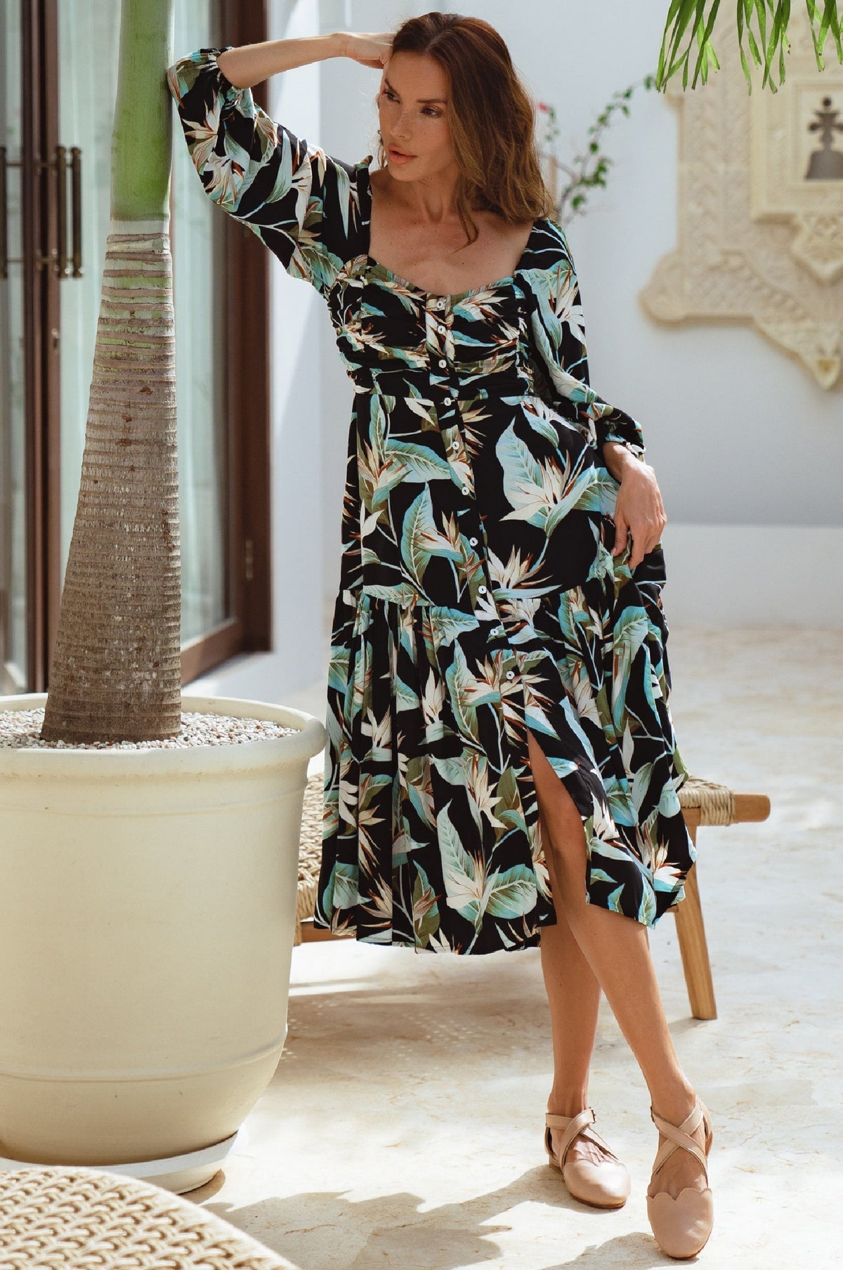 Woman in a floral dress standing in a bright room with plants.