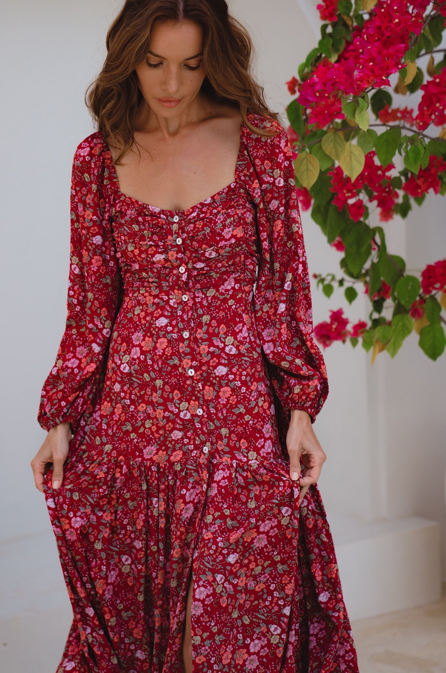 Woman wearing a red floral dress standing next to a plant with red flowers.
