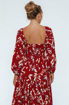 Woman wearing a red floral dress with a plain background back view