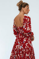 Woman wearing a red floral dress with a plain background 3/4 view
