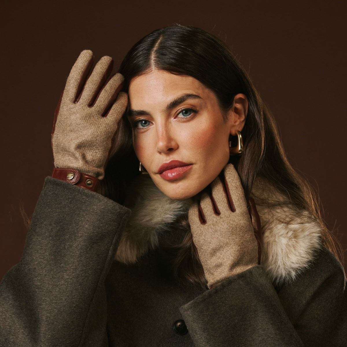 Woman wearing a coat with fur collar and gloves against a brown background