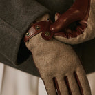 Close-up of a person wearing brown leather gloves with a coat button, on a neutral background.