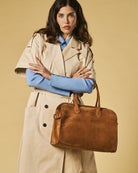 Woman holding a brown leather bag against a beige background