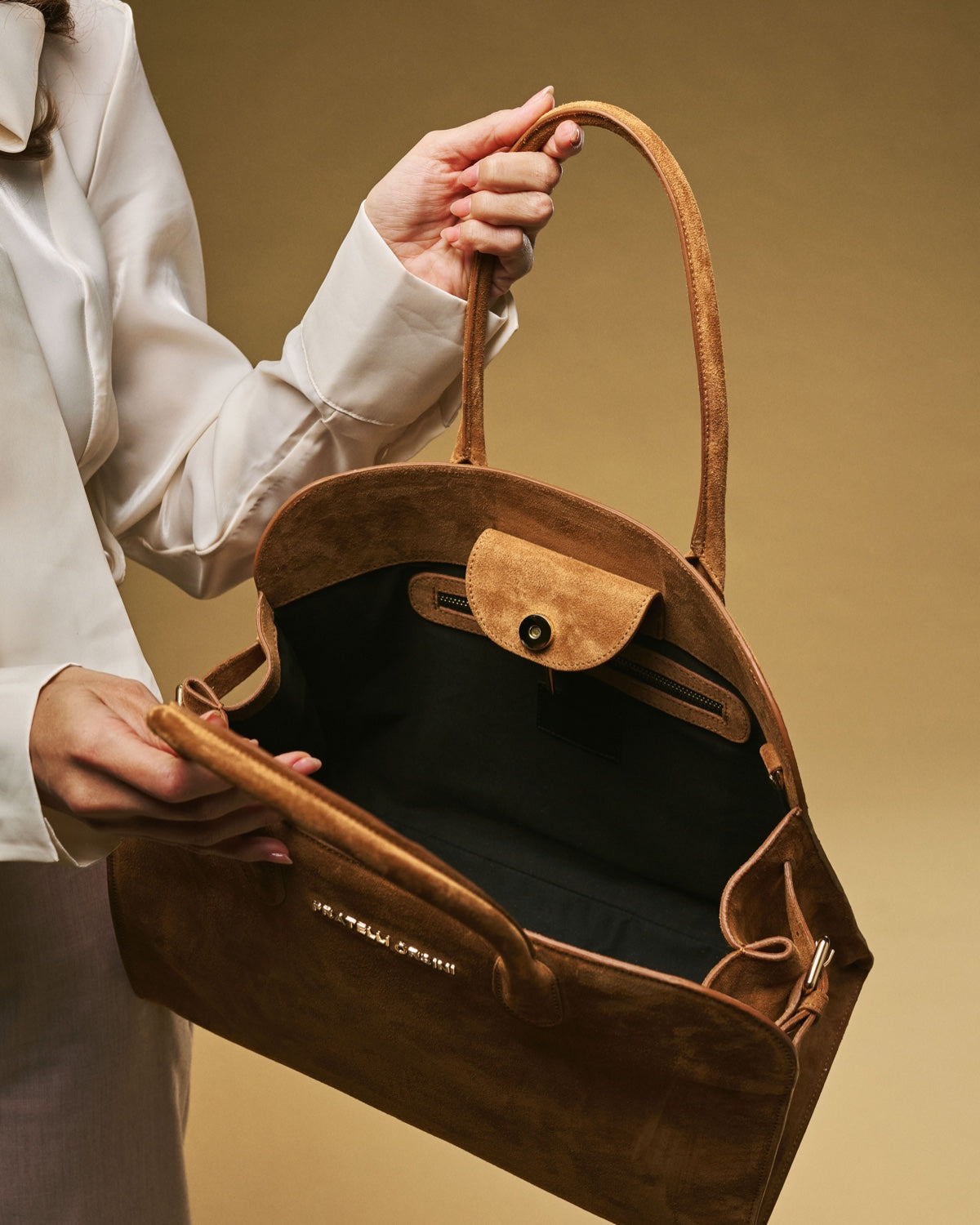 Brown leather handbag held by a person against a beige background