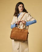 Woman holding a brown leather bag against a beige background