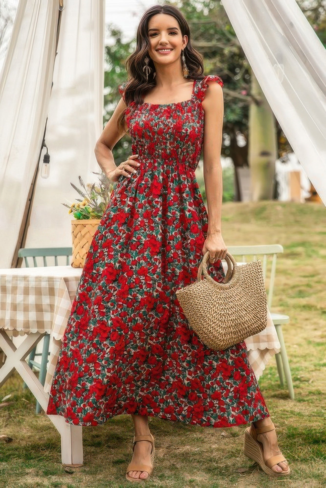 Model in a red floral dress holding a straw bag outdoors.