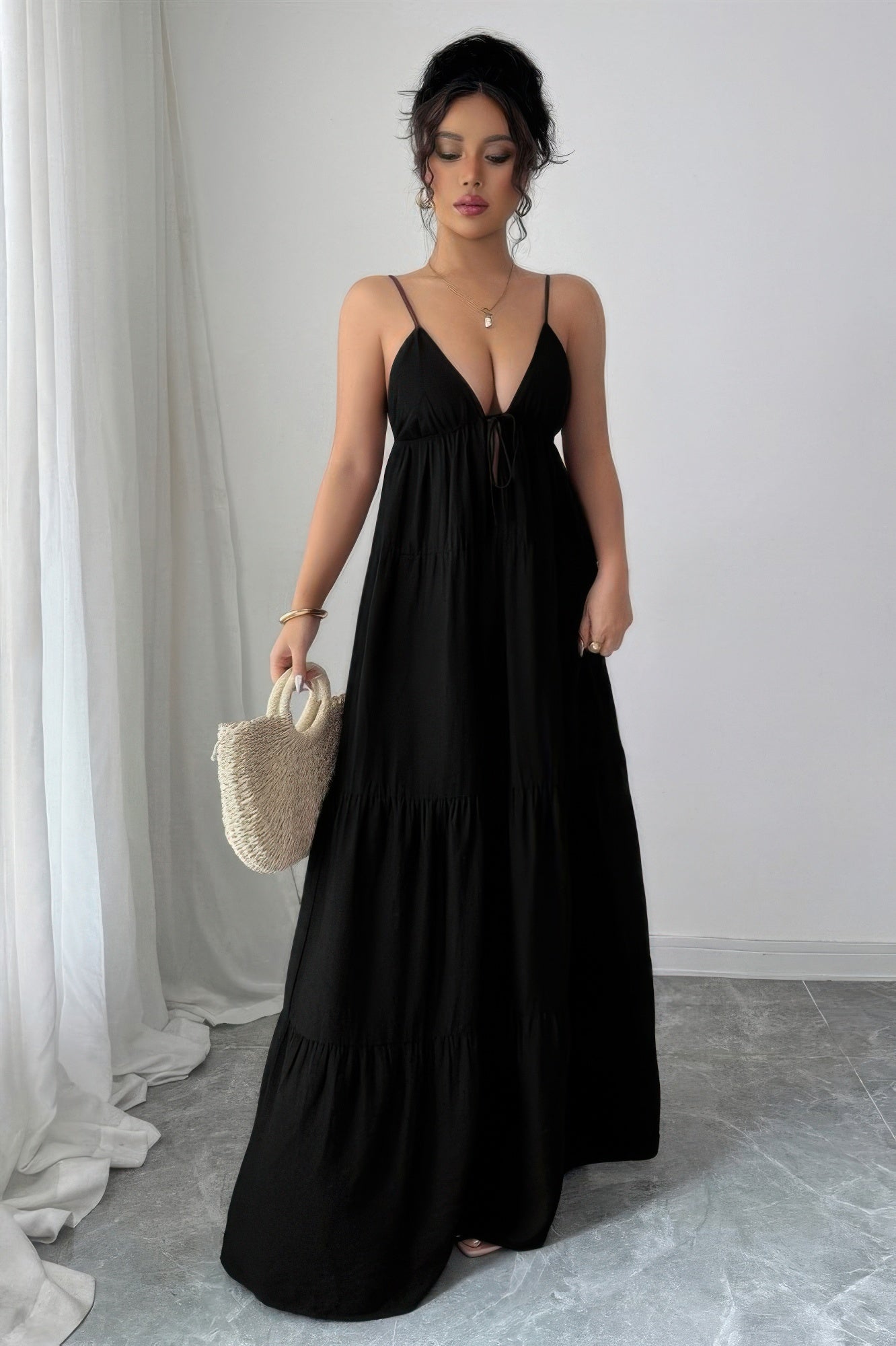 Woman wearing a black tiered maxi dress with adjustable spaghetti straps, plunging V neckline, empire waist, and flowing tiered skirt.