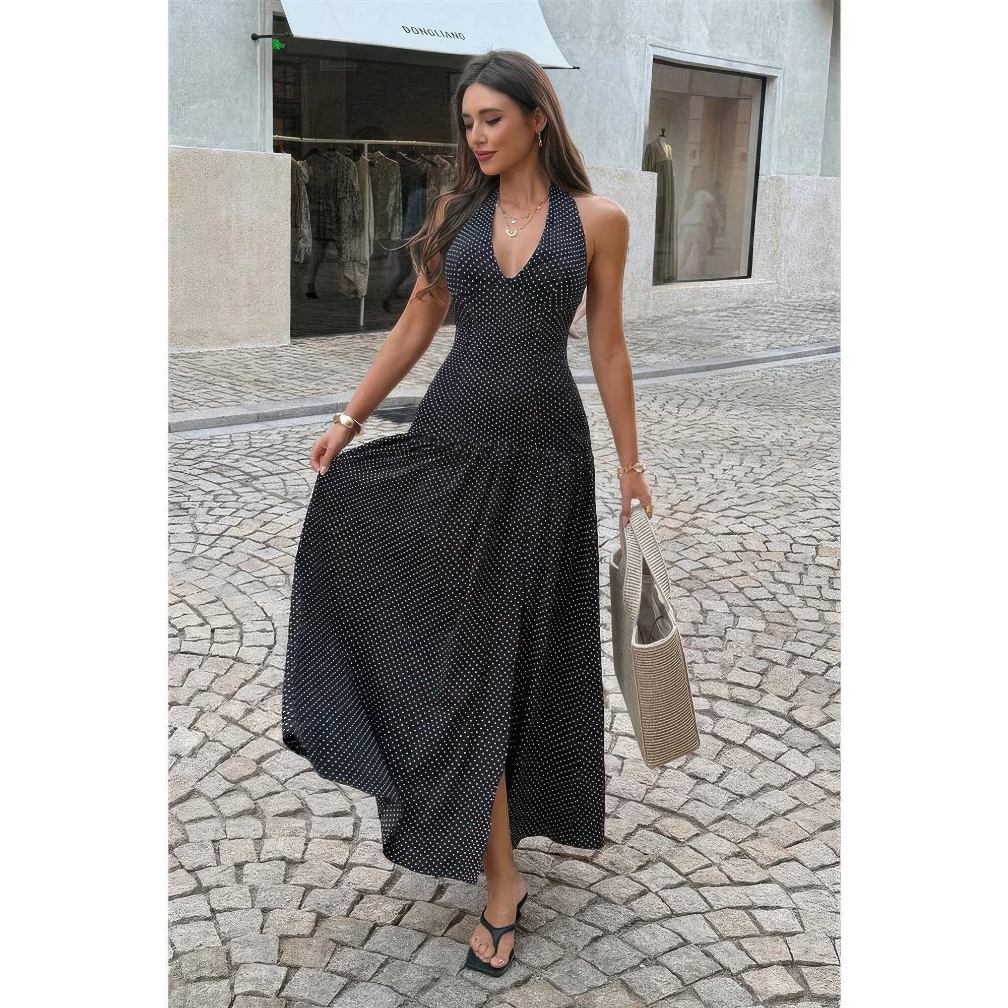 Model wearing black polka dot halter maxi dress with open back and front slit.
