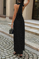 Woman wearing long black with maxi dress with white polka dots with halter and deep v-neckline back view
