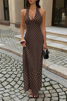 Woman wearing long chocolate brown with maxi dress with black polka dots with halter and deep v-neckline, in front of restaurant window