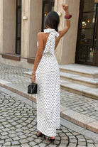 Woman wearing long white with maxi dress with black polka dots with halter and deep v-neckline, back view